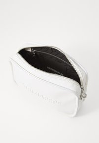 Funda de piel blanca con cremallera y logotipo en relieve, textura suave y un interior con patrón oscuro. Presenta herrajes plateados para el cierre.