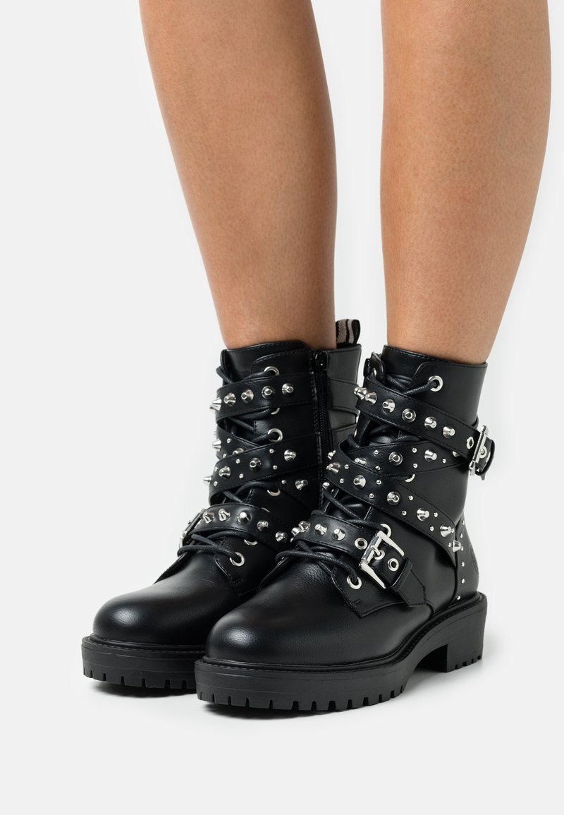 Bottes noires en cuir avec des clous et des boucles argentés, dotées d'une semelle épaisse et d'un design à lacets.