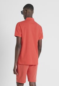 Rode katoenen polo met een kraag, korte mouwen en bijpassende shorts, beide met een gladde textuur en een minimalistisch ontwerp.