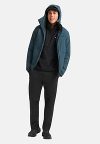 Completo a due pezzi con giacca imbottita teal con cappuccio, pullover in pile nero, pantaloni neri e scarpe da ginnastica scure e texturate.