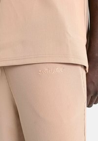 Lichtbeige geribde trui en broek met borduursel met de tekst "SIXTH JUNE." De stof heeft een gladde, getextureerde uitstraling.