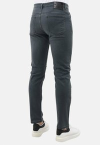 Grijze slim-fit jeans voor heren met een zachte textuur, voorzien van een zwart logo op de tailleband en achterzakken. Gemaakt met witte en zwarte sneakers.
