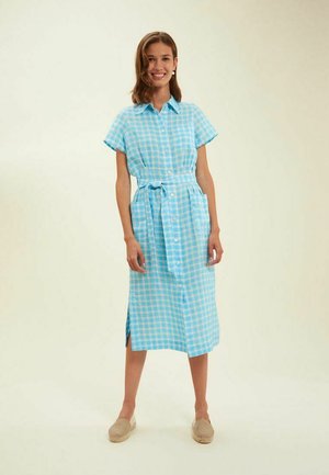 Robe chemise à carreaux bleus avec des manches courtes, fermeture à boutons sur le devant, ceinture à la taille et fentes latérales. Fabriquée en tissu léger, idéale pour un style décontracté.