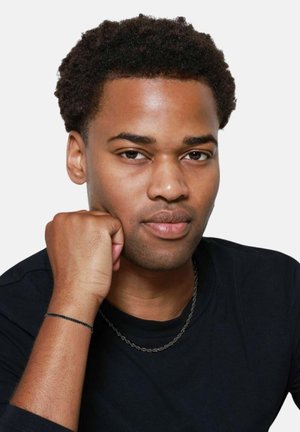 Portrett av en person med kort, krøllete hår som har på seg en svart crew-neck skjorte. Merker inkluderer et svart kjede rundt halsen og et armbånd.