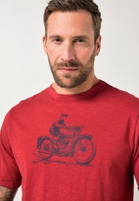 Červené bavlněné tričko s vintage grafikou motocyklu v tmavě modré barvě. Kulatý výstřih a krátké rukávy. Strukturální látka s mírným melírováním.