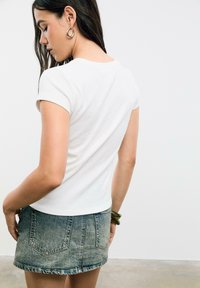 T-shirt blanc ajusté à manches courtes et col rond. Associé à une mini-jupe en denim clair. Tissu lisse avec peu de détails de design.