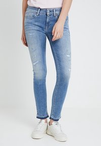 Jeans ajustados de color azul claro con acentos desgastados y secciones deslavadas. Hechos de denim, cuentan con un diseño clásico de cinco bolsillos y cierre de botón.