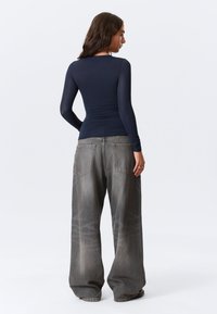 Marineblauw top met lange mouwen gecombineerd met loszittende, vervaagde grijze jeans met achterzakken en een gladde textuur.