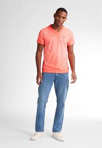 Korallinvärinen V-pääntie T-paita hienovaraisella tekstuurilla, yhdistetty vaaleansinisiin farkkuihin. Asun viimeistelevät valkoiset tennarit rentoon tyyliin.