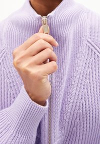 Vaaleanlila neulottu vetoketjullinen villapaita, jossa on korkea kaulus. Varustettu hopeisella vetoketjulla ja ribbireunoilla, joka esittelee teksturoituja ompelupintoja.