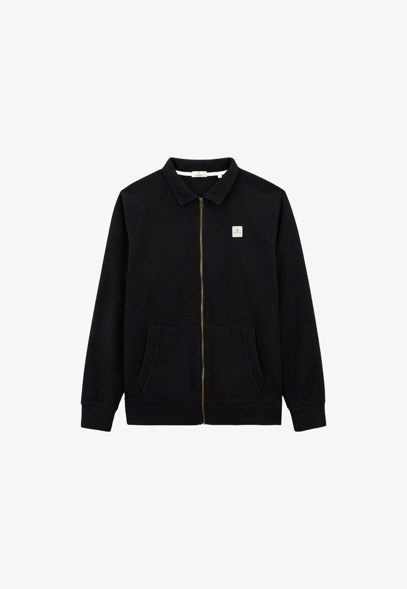 Veste noire zippée en tissu doux, dotée d'un col pointu, de deux poches avant et d'une petite patch logo sur la poitrine.