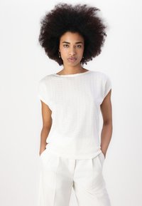 White, textured top with short sleeves, rounded neckline, and a relaxed fit, paired with white high-waisted trousers.