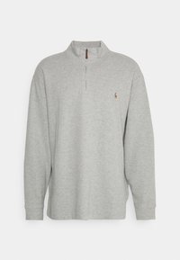 Ljust grå långärmad tröja med halvdragkedja och liten broderad logotyp på vänster bröst.