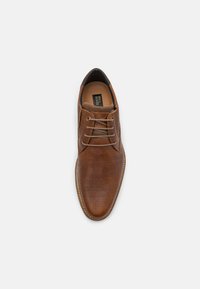 Chaussure habillée en cuir marron avec un design perforé, bout rond et lacets. Caractéristiques incluent une texture lisse et des accents tonaux.