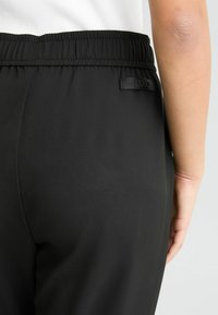 Schwarze Hose aus glattem Material mit elastischem Bund, ausgestattet mit einem kleinen LIU JO-Label auf der Rückseite. Schlichtes Design, keine sichtbaren Muster.