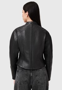 Giacca di pelle nera con un design aderente, cuciture delle spalle in vista e una texture liscia. Nessuna hardware o motivo visibile.