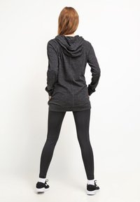 Black long-sleeve hoodie with a textured fabric and a hood, paired with black leggings and black sneakers, viewed from the back.