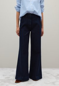 Jeans a gamba larga blu scuro con vita alta, realizzati in denim. Presentano una chiusura con bottone e zip, e tasche anteriori e posteriori.
