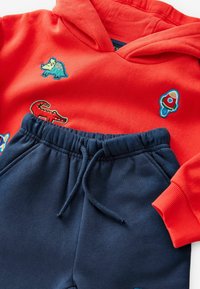 Rød hættetrøje med broderede dyre- og raketdesigns, parret med marineblå sweatpants med elastisk talje og snøre.
