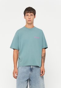 Teal cotton t-shirt with short sleeves and a crew neck. Features pink text "work hard, save harder" on the left chest area. Casual fit.