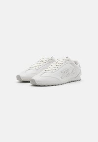 Hvite atletiske sneakers med teksturert skinn, snørebånddesign, gummisåler og brodert logo detalj på siden.
