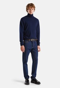 Maglione a collo alto blu abbinato a jeans scuri, con una cintura nera e scarpe nere lucide con suola spessa.