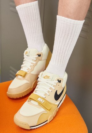 Nike sportovní boty ve béžové a krémové kůži, s černým swooshem, bílými tkaničkami, suchým zipem a texturovanou gumovou podrážkou.