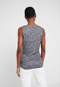 Šedé bezrukávové tílko s texturovaným, melírovaným pleteným vzorem. Má zaoblený výstřih a přiléhavý střih, lem mírně klesá vzadu.