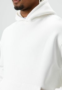 Witte sweatshirt met capuchon, voorzien van een zachte textuur en een ruime pasvorm. Voorzien van een zak aan de voorkant en gestikte accenten.