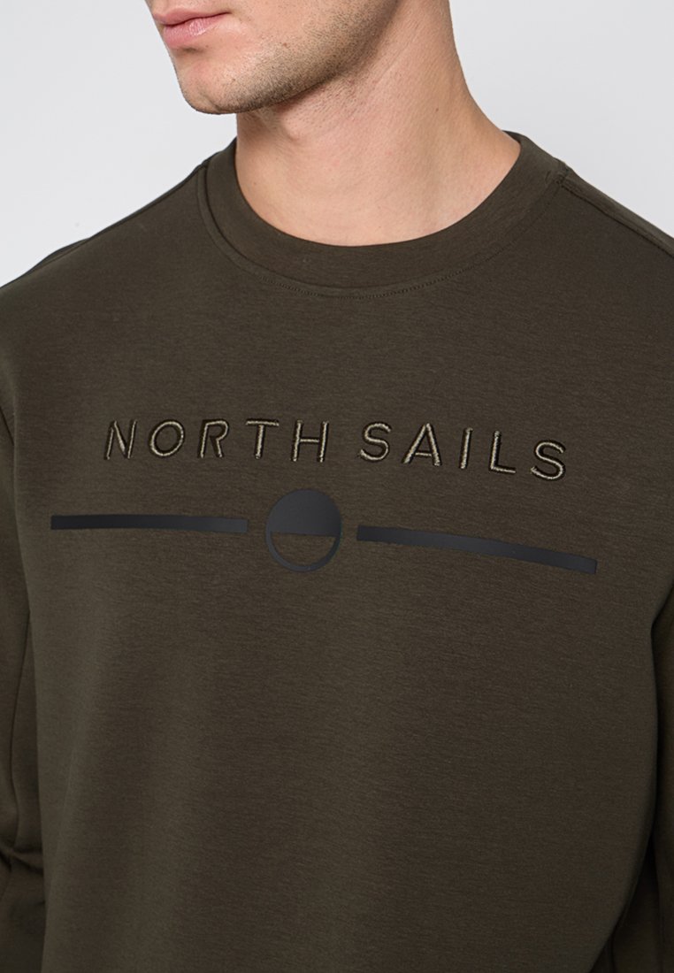 Uomo che indossa un felpa verde oliva scuro con il testo "NORTH SAILS" e una linea orizzontale con un logo a mezzaluna sotto il testo.