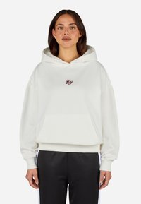 Sudadera color crema hecha de material suave, con un gran bolsillo frontal, puños acanalados y un pequeño logo rojo en el pecho.