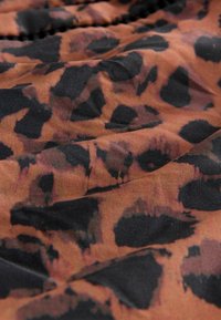 Tkanina s životinjskim uzorkom koja sadrži smeđe i crne leopard točkice na mekoj, teksturiranoj površini, s suptilnim varijacijama u boji i uzorku.