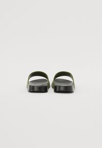Sandale negre cu un brâu verde, cu talpă plată și design deschis la spate, realizate dintr-un material mat, neted.