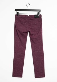 Burgundy snäva byxor med ett subtilt mönster. Har två bakfickor och en etikett märkt "A.J." på midjebandet, hängande på en svart galge.