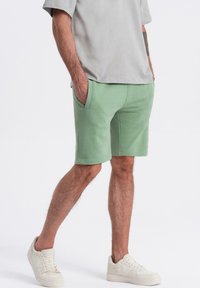 Shorts vert menthe en mélange de coton, avec une taille élastique, des poches latérales et une coupe décontractée. Associés à des baskets blanches.