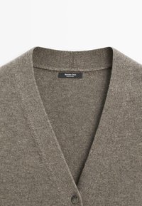 Šedý vlněný cardigan s výstřihem do V, s texturovaným pletením a jediným černým knoflíkem na zapínání. Na štítku je nápis "Massimo Dutti."