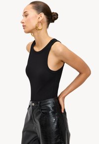 Top de tirantes negro acanalado con cortes amplios, combinado con pantalones de cuero sintético negro de cocodrilo de tiro alto con cierre de botón.