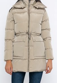 Beige Pufferjacke mit hohem Kragen, tailliertem Schnitt und zwei vorderen Taschen. Der glatte, glänzende Stoff hat ein horizontales Steppmuster.