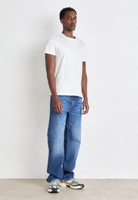 Vit kortärmad t-shirt i kombination med avslappnade blå jeans och grå sneakers. Jeansen har en blekt textur och rak passform.