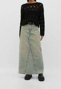 Zwarte gebreide trui met open structuur, gecombineerd met een lange lichtblauwe denim rok met een voornaaddetail en een hoge taille. Zwarte plateau laarzen.