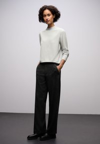 Helle graue Langarmpullover mit hohem Kragen, kombiniert mit lockeren, hochtaillierten schwarzen strukturierten Hosen und schwarzen klobigen Schuhen.