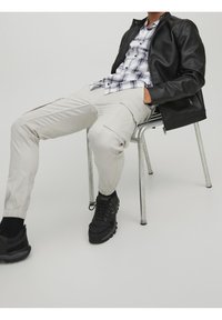 Mustat nahkasateenkaarijakki valkoisen ja sinisen ruutupaidan päällä, yhdistettynä vaaleanbeigeihin jogger-housuihin ja mustiin paksupohjaisiin lenkkareihin.