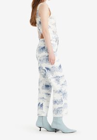 Conjunto de jean con un estampado paisajístico en azul y blanco; top ajustado con tirantes anchos, pantalones de pierna ancha de talle alto y botas de tobillo puntiagudas en azul claro.