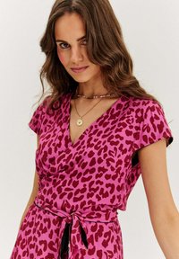 Fučková šaty s v-výstrihom, krátkymi rukávmi a zvieracím vzorom v tmavších odtieňoch. Viazaný pás pridáva tvar a záujem o dizajn.