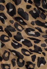Tkanina s leopardím vzorom v znamení béžového pozadia s veľkými čiernymi škvrnami a menšími bielymi akcentmi, hladká textúra a mierne priesvitná kvalita.