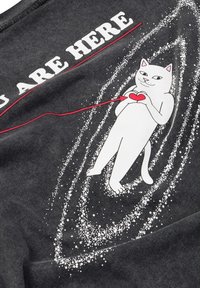 Czarna tkanina z grafiką białego kota z czerwonym sercem, otoczonego wzorem galaktyki z białych kropek. Tekst brzmi: "JESTEŚ TU."