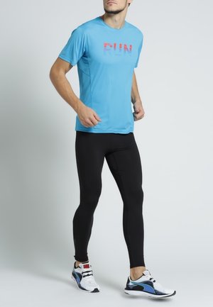 Ljusblå tränings t-shirt med "RUN" tryckt i röd och blå gradient, matchad med svarta leggings och vita sneakers med blå accenter.