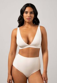Helle beige Zweiteiler bestehend aus einem tief ausgeschnittenen Bralette mit dünnen Trägern und einer hochgeschnittenen Hose. Weicher, strukturierter Stoff mit einer glatten Oberfläche.