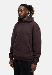 Dunkel lila Kapuzenpullover mit großer Kapuze, Fronttasche, lockerer Passform und gerippten Bündchen. Tragen mit dunkler Jeans.