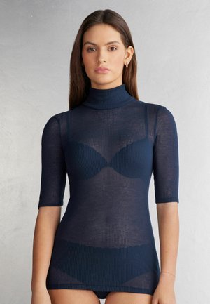 Haut à col roulé côtelé bleu marine à manches courtes ; la texture transparente révèle un sous-vêtement sombre en dessous. Fini lisse et design ajusté.